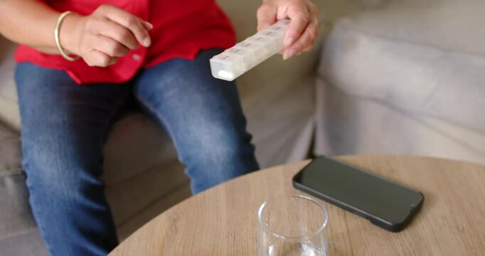 Senior Asian woman reaching, lifting pillbox from coffee table, opening slots and checking doses