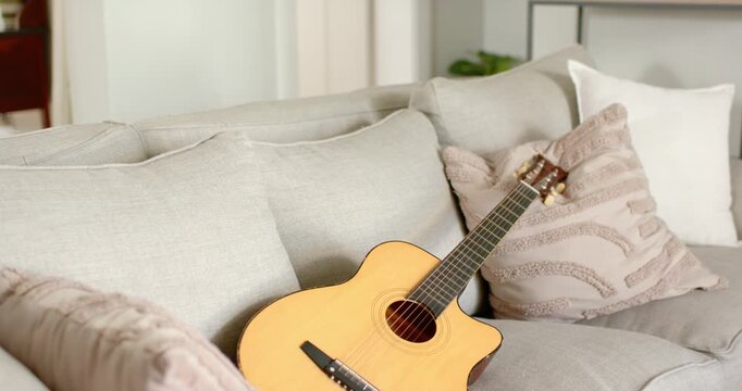 Camera is panning right revealing acoustic guitar on sofa, neck rising and headstock showing detail