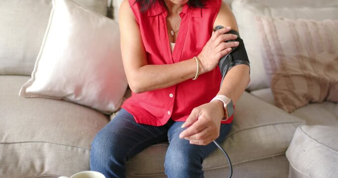 Senior Asian woman in red blouse wrapping cuff, linking monitor, checking BP reading with beeping