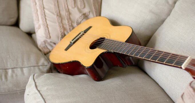 Camera is adjusting framing and focus, moving closer and centering acoustic guitar on beige sofa