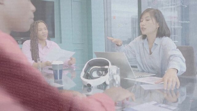 Speaker leading tech meeting at glass table, colleague typing, overlays showing helmet proto review