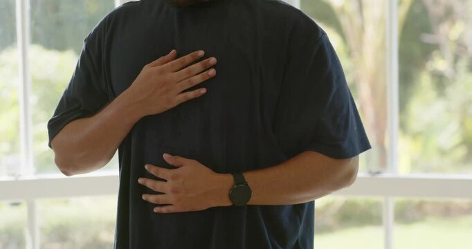 Mid adult African American man placing hands on chest and abdomen, warming voice by window