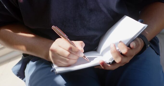 Mid-adult African American man positioning spiral notebook writing notes with rose-gold pen at home