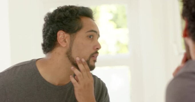 Mid-30s African American man leaning at mirror tracing beard and checking eye area in gray tee