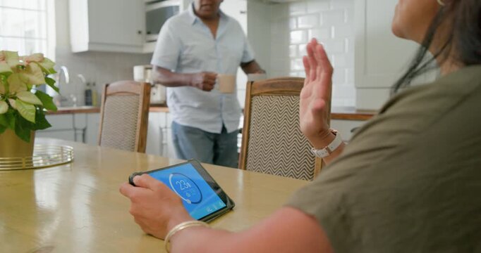 African American couple at kitchen table, woman tapping tablet urging man to join to check temp