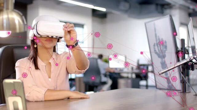 Woman sitting at desk initiating reach, manipulating pink hexagonal VR nodes for tech prototyping