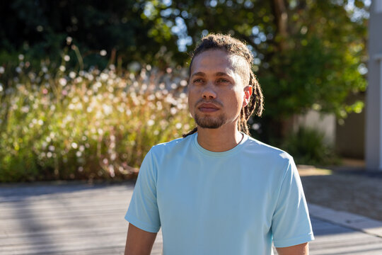 African American man standing on wood deck wearing light blue tee, gazing up at tall grasses