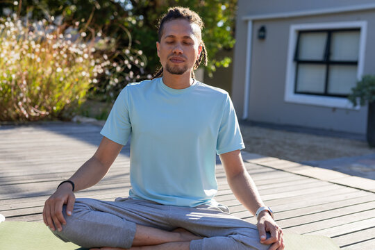 African American man meditating on green mat on deck wearing light-blue T-shirt, wristwatch