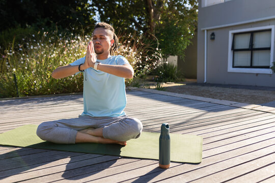 African American man meditating hands pressing at chest on green mat on deck, water bottle nearby