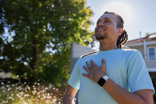 African American man standing hand on chest looking up yard wearing shirt smartwatch, copy space