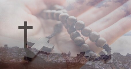 Obraz premium Holding open palm, adult hand cradling wooden rosary beads over rocky hilltop silhouetted cross