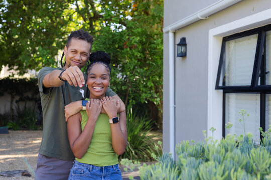 African couple handing keys to camera while wearing watches in front yard on gravel pathway
