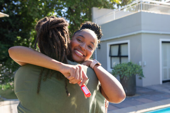 African American couple hugging, woman holding red key fob and smartwatch on tiled patio