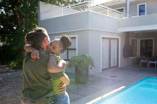 African American couple embracing beside modern two-story house by pool, man holding red key fob