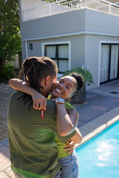 African American couple hugging patio by pool, man holding red key fob, woman with white smartwatch