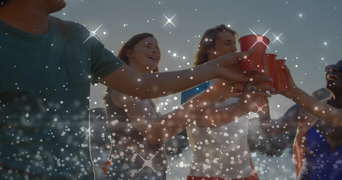 Clinking red disposable cups, group of five friends toasting at shoreline, wearing summer clothes