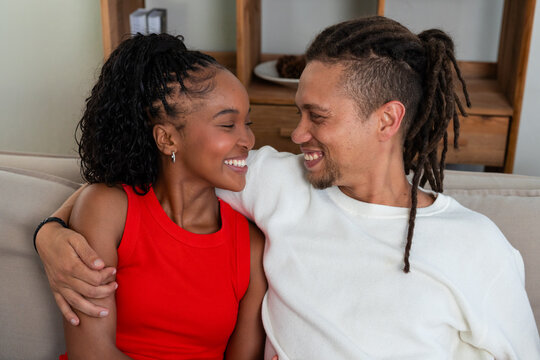 African American couple leaning on sofa near wooden shelf at home, wearing white and red tops