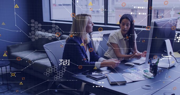 Collaborating two colleagues in navy blazer pointing at desktop monitor and papers in modern office