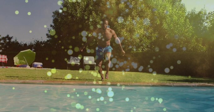 Running adult shirtless man in blue swim trunks heading toward pool at backyard lawn, with umbrella