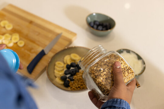 African American man holding clear jar making granola bowl with banana and blueberry on counter