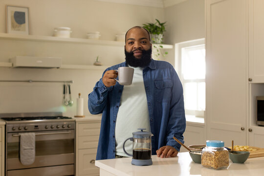 African man standing at kitchen island holding ceramic mug and resting hand by French press