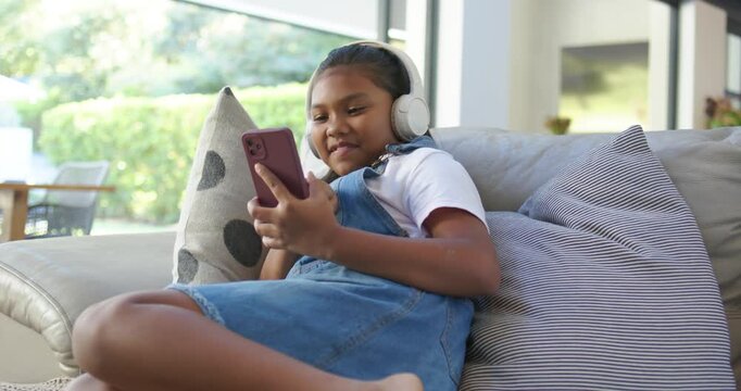 African American child receiving alert, tapping, scrolling purple phone lying on sofa with headset