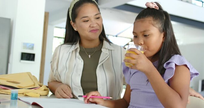 Diverse mother and child doing homework with pink pencil using tablet while mom guiding at counter