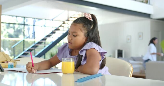 African American girl child sitting at kitchen island, writing with pink pencil, studying worksheet