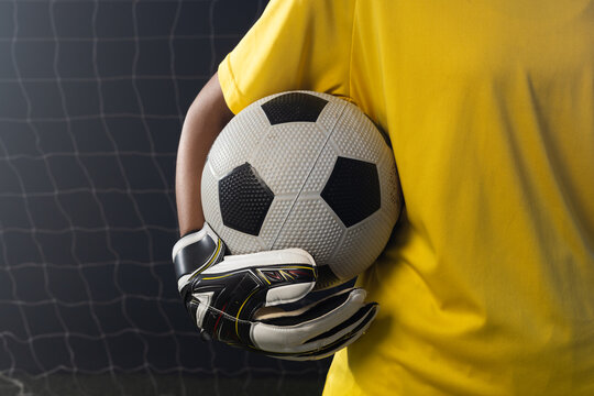African American woman goalie holding soccer ball with padded gloves at goal net in yellow jersey