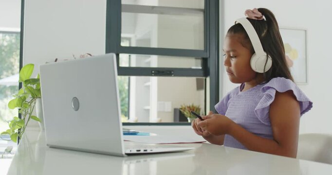 African American girl hearing lesson via headphones at table with laptop, taking notes, copy space