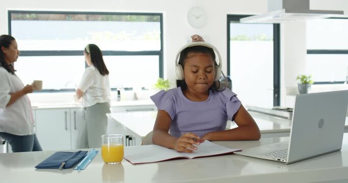 Female family preteen girl writing notebook at kitchen island, adults talking behind causing glance