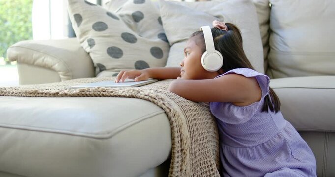 African American girl child with headset kneeling at ottoman, tapping tablet after ping, copy space