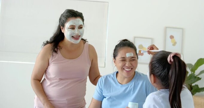 Diverse females at home, masked woman holding jar urging child brushing with flat brush for fun