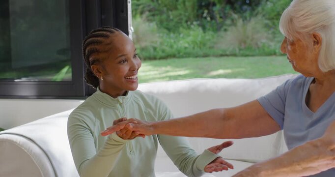 African-American carer placing hand under arm guiding senior through arm lifts on sofa for balance