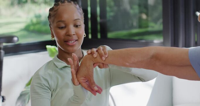 African American carer guiding senior's forearm on sofa during therapy, rotating wrist for mobility