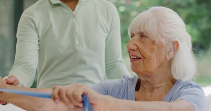 Caregiver and Senior woman doing rehab, caregiver placing blue band while Senior pulling by window
