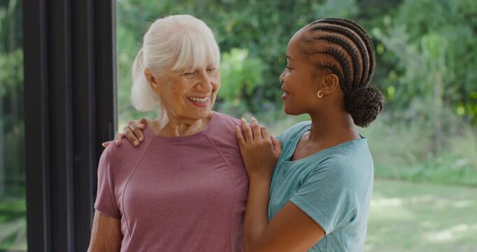 Female relatives, African woman placing hands on senior, laughing warmly at door, mauve teal shirts