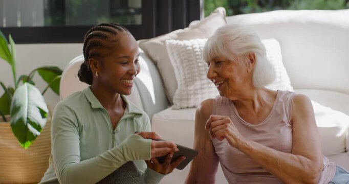Female African American carer holding tablet showing screen to Senior on floor at home highfiving