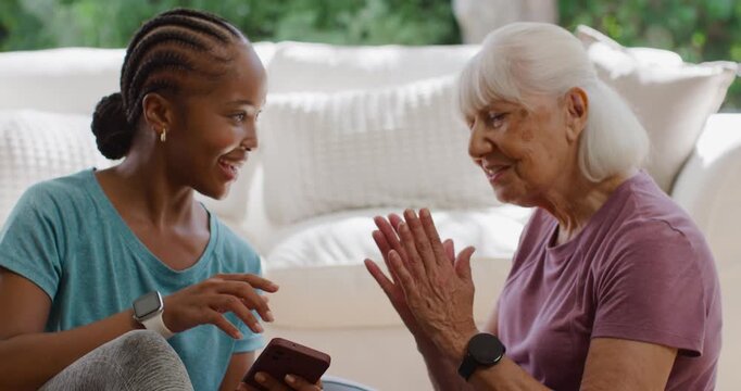 African American woman showing phone, senior woman clapping and giving thumbs-up on sofa, cheering