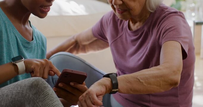 African American woman caregiver pointing at phone, guiding senior woman checking tracker at home