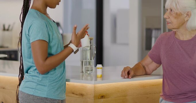 Diverse caregiver reacting to pill bottle showing dispenser explaining dosage to senior in kitchen