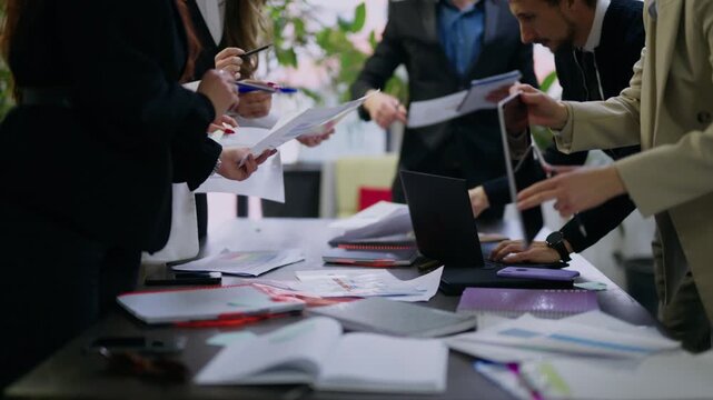 A group of business professionals are actively engaged in a meeting, reviewing documents and utilizing a laptop.