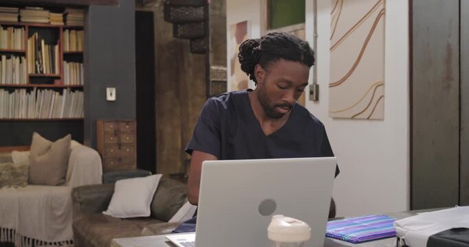 Man navy-scrubs working on laptop at counter pulling blue sleeve from bag filing papers into folio