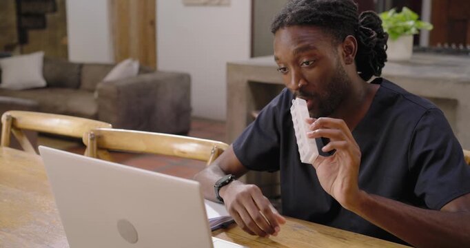 Adult African man in scrubs seeing laptop, checking bottle and swab at wooden table entering data