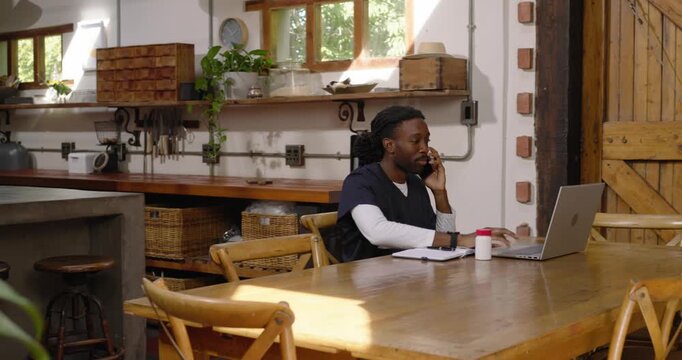 African American man taking call, typing laptop checking notes for work at rustic table, copy space
