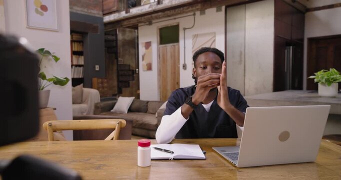 Man in scrubs sitting at table, aligning to DSLR appearing, glancing at laptop, showing pill bottle