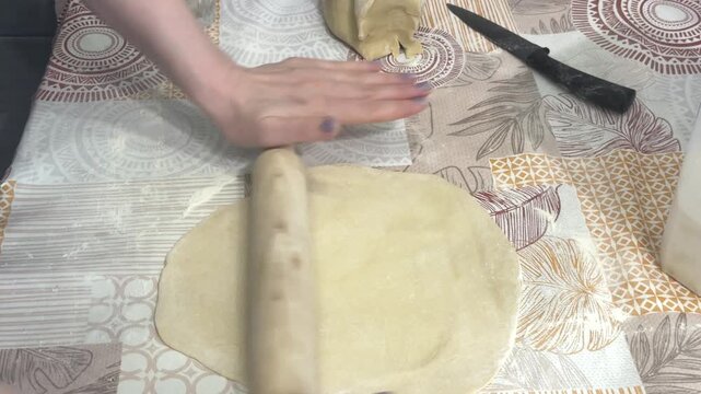 A woman rolls out a large sheet of raw dough and folds it in half, home kitchen setting. Homemade pastry preparation, traditional baking, culinary process.