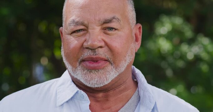 Senior man starting to speak, smiling while replying to question in garden wearing light blue shirt