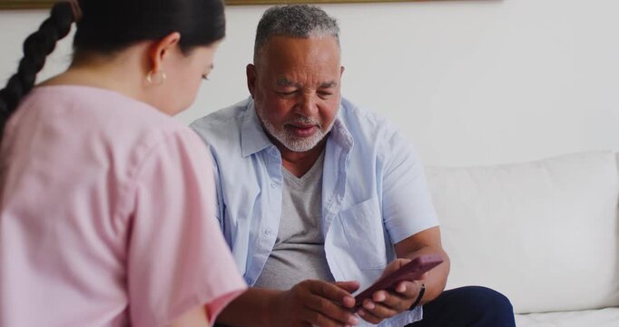 Senior African American man tapping pink phone, drawing Adult Asian woman closer on white couch
