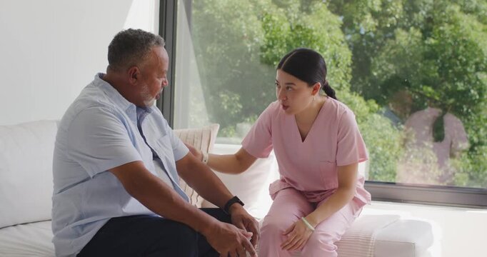 Asian nurse, pink scrubs assisting Sr African-American man rising from sofa for backache after talk
